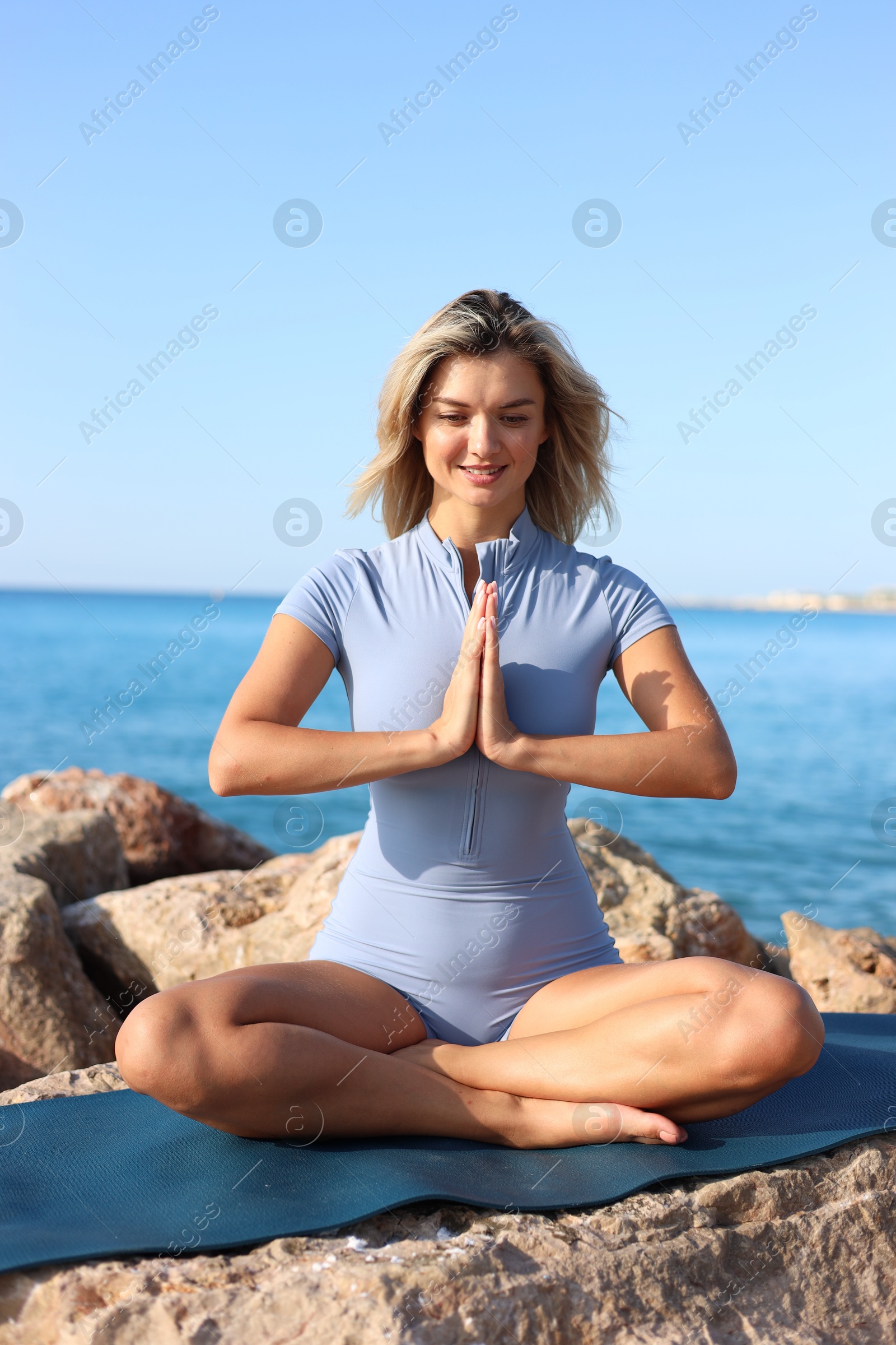 Photo of Young woman in sportswear practicing yoga on rocks at beach