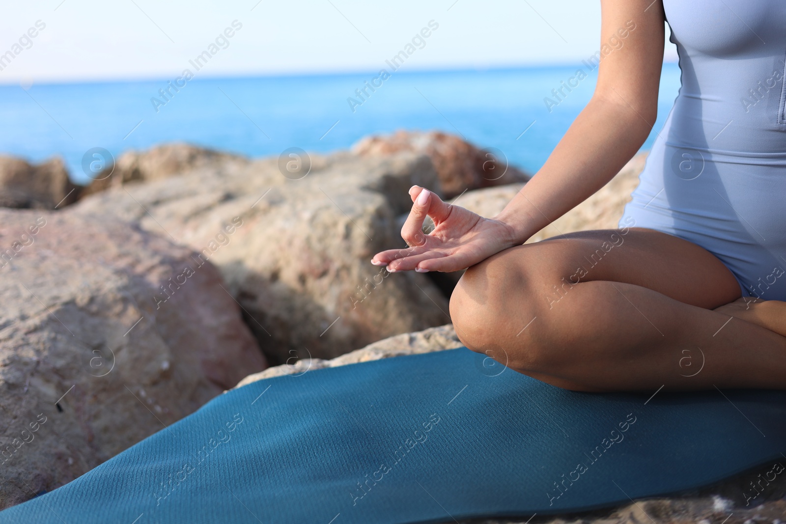 Photo of Young woman in sportswear practicing yoga on rocks at beach, closeup. Space for text