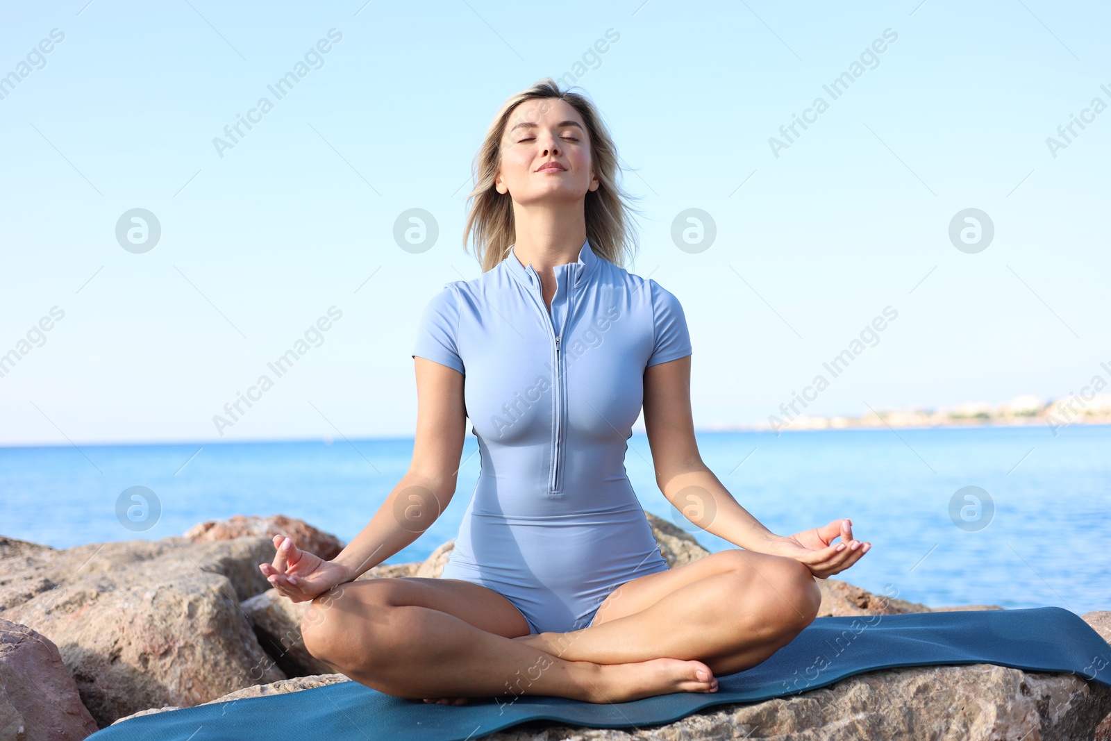 Photo of Young woman in sportswear practicing yoga on rocks at beach