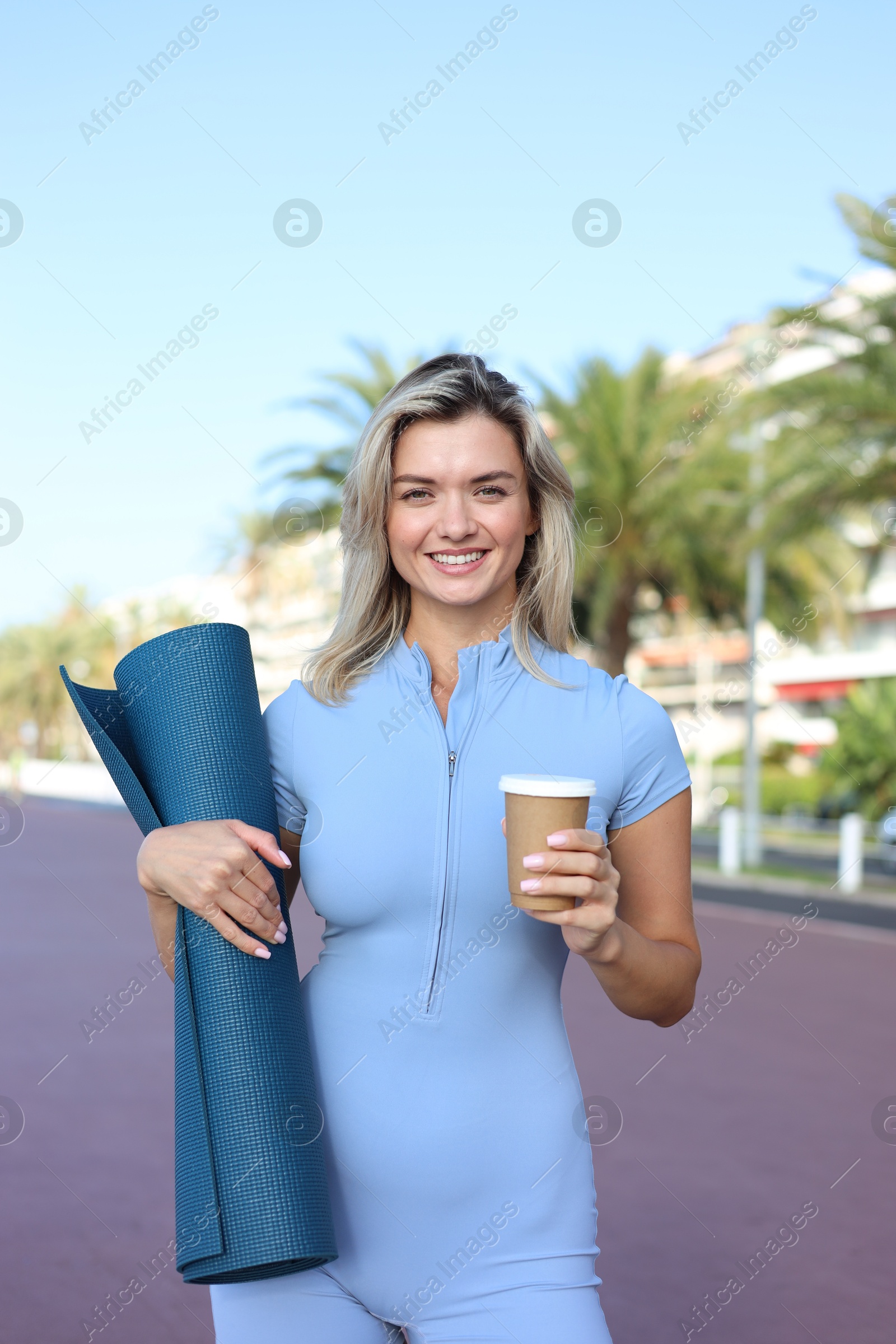 Photo of Happy young woman with yoga mat and cup of drink outdoors