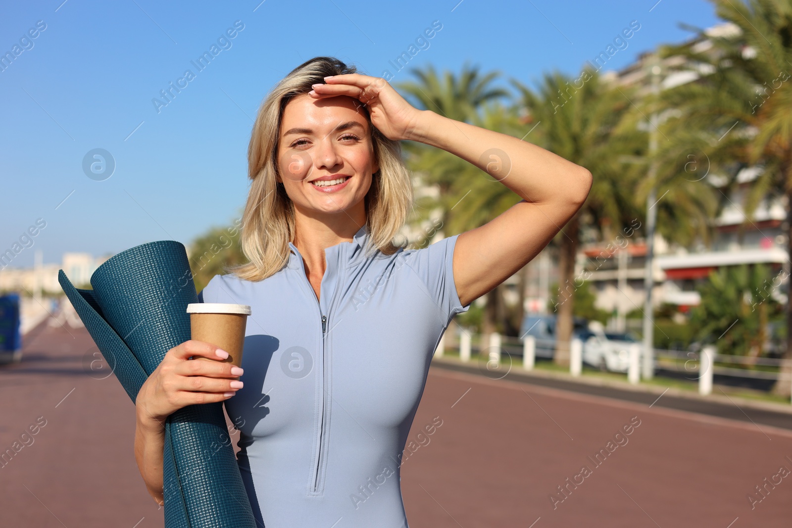Photo of Happy young woman with yoga mat and cup of drink outdoors, space for text