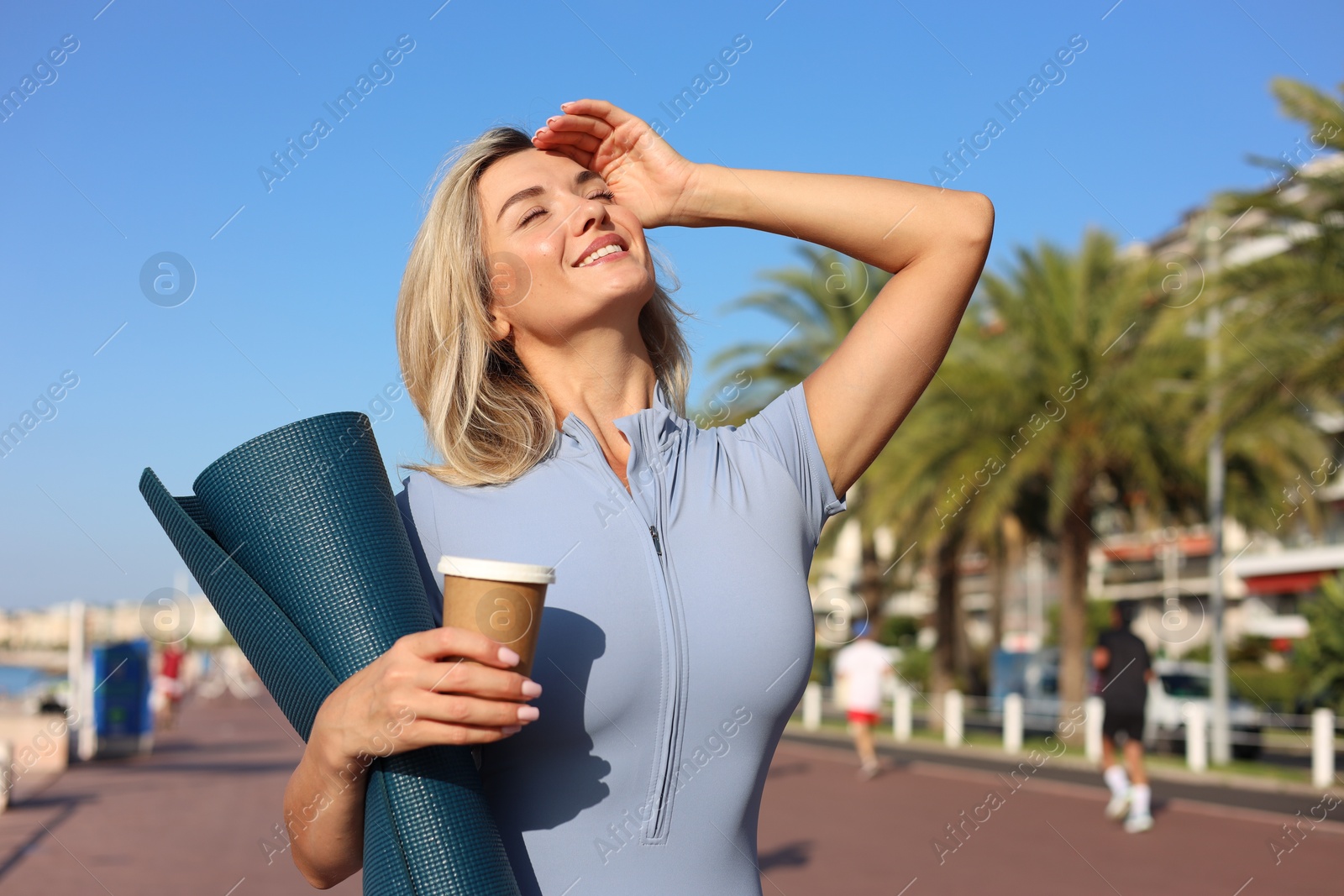 Photo of Happy young woman with yoga mat and cup of drink outdoors