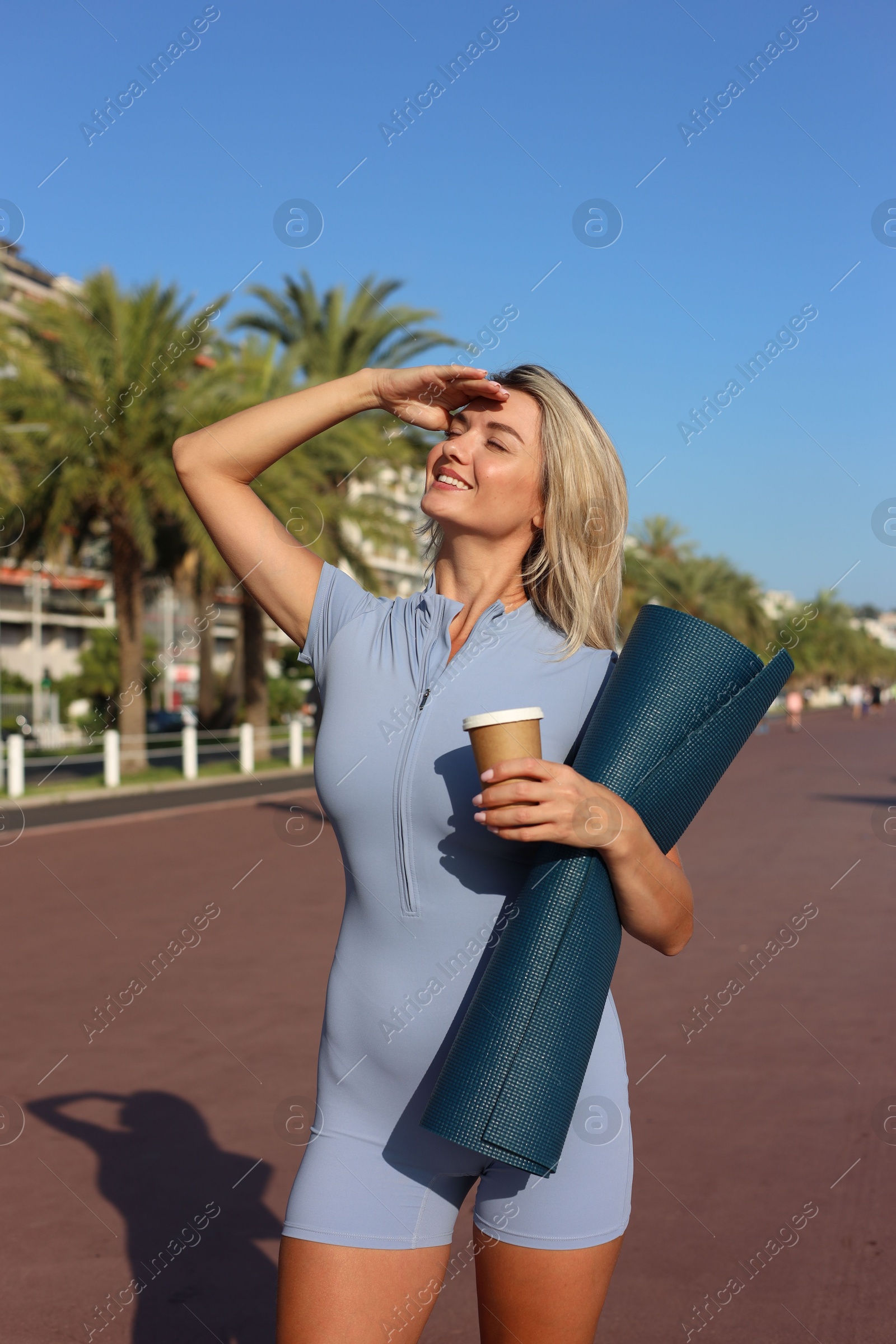 Photo of Happy young woman with yoga mat and cup of drink outdoors