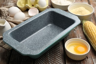 Photo of Making cornbread. Baking dish and different ingredients on wooden table, closeup