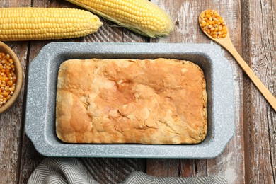 Photo of Freshly baked cornbread in baking dish, cobs and spoon on color wooden table, flat lay