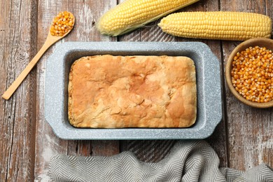 Photo of Freshly baked cornbread in baking dish, cobs and spoon on color wooden table, flat lay