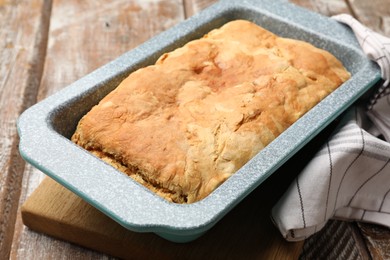 Photo of Freshly baked cornbread in baking dish and napkin on color wooden table, closeup