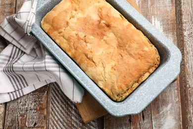 Photo of Freshly baked cornbread in baking dish and napkin on color wooden table, top view