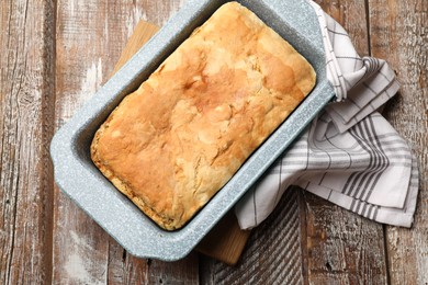 Photo of Freshly baked cornbread in baking dish and napkin on color wooden table, top view