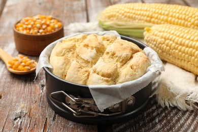 Photo of Freshly baked cornbread in cake pan, cobs and napkin on color wooden table, closeup