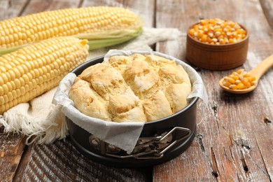 Photo of Freshly baked cornbread in cake pan, cobs and napkin on color wooden table, closeup