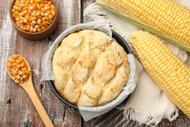 Photo of Freshly baked cornbread in cake pan, cobs and spoon on color wooden table, flat lay