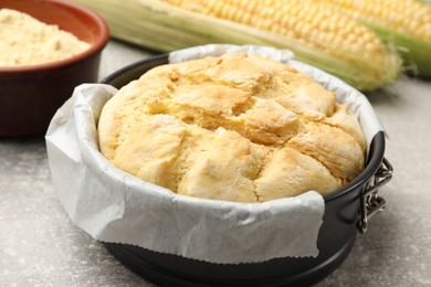 Photo of Freshly baked cornbread in cake pan on grey textured table, closeup