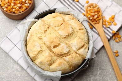 Photo of Freshly baked cornbread in cake pan, seeds and spoon on grey textured table, flat lay