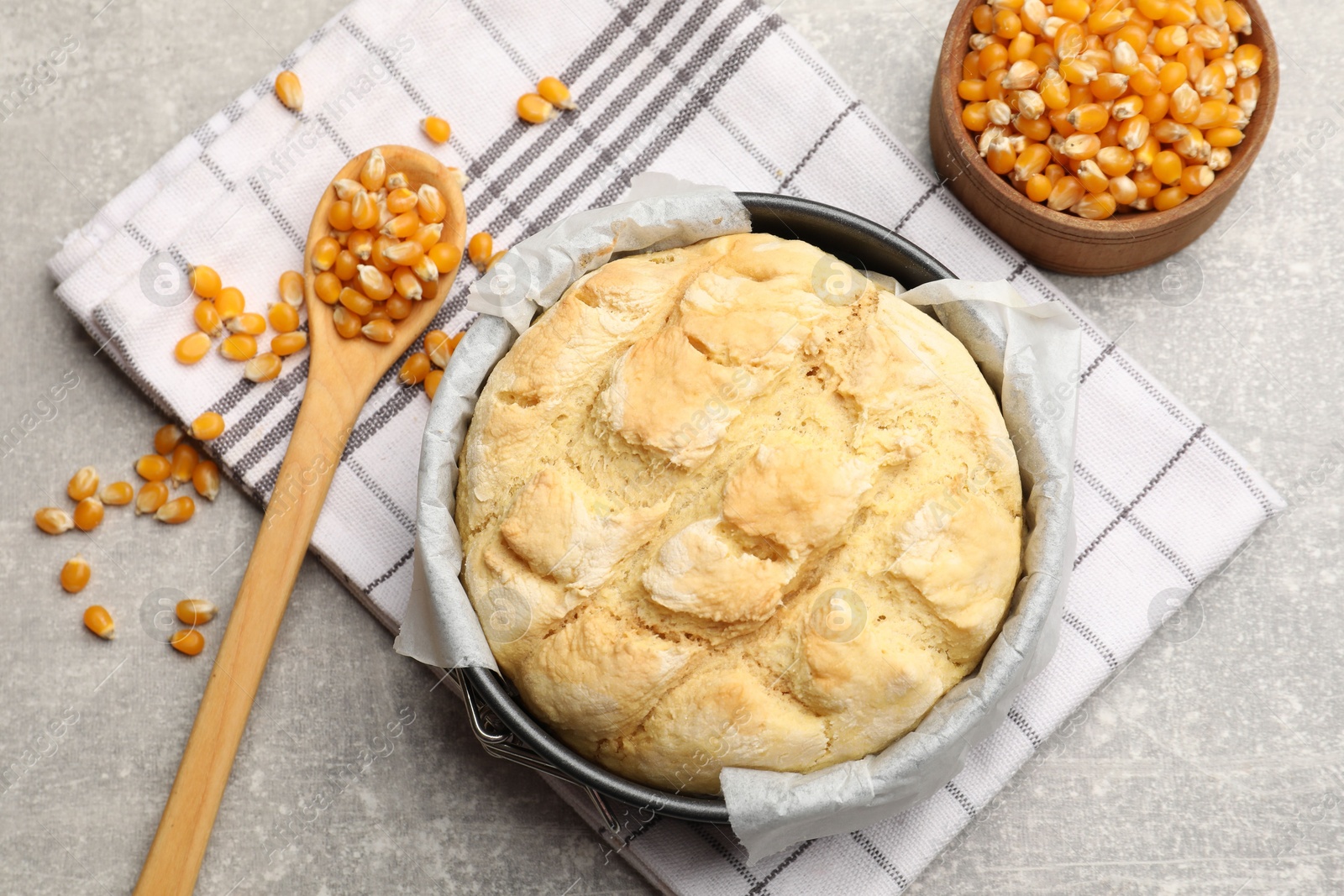 Freshly baked cornbread in cake pan, seeds and spoon on grey textured table, flat lay Photo of Freshly baked cornbread in cake pan, seeds and spoon on grey textured table, flat lay