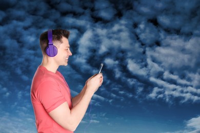 Image of Happy man listening to sounds of nature which making him feel calm. Blue sky with clouds on background