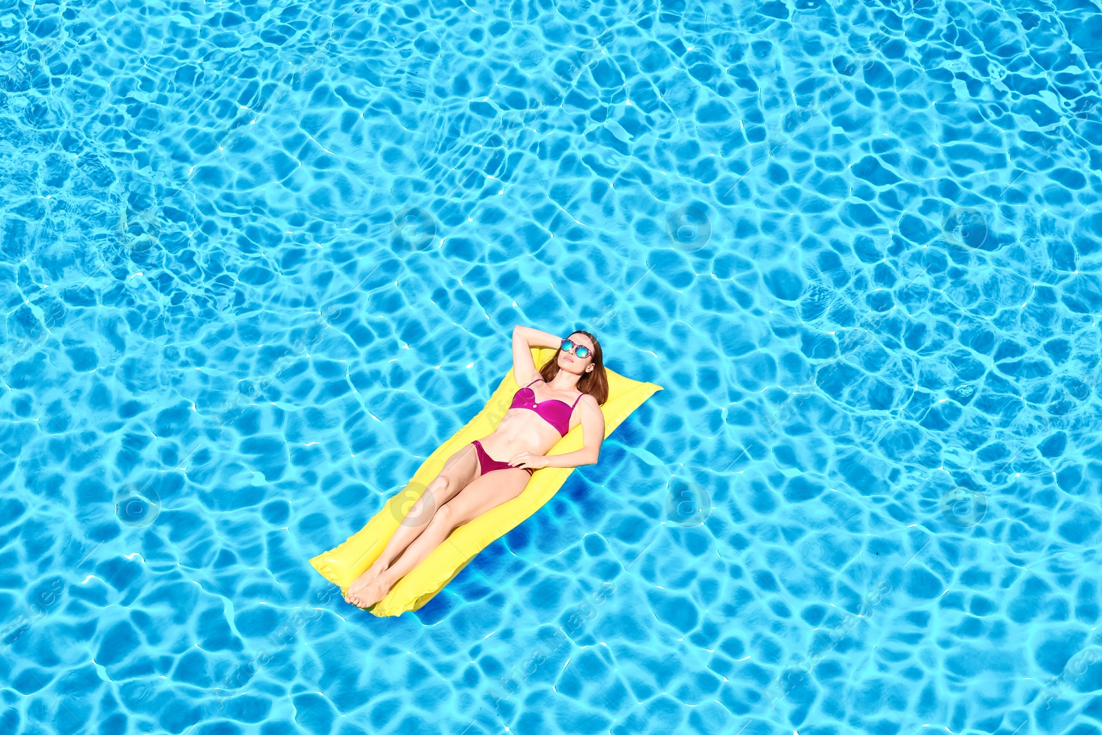 Image of Young woman on inflatable mattress in swimming pool, above view