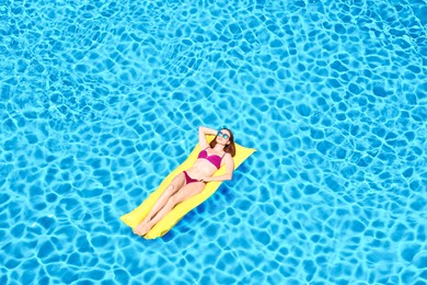 Image of Young woman on inflatable mattress in swimming pool, above view