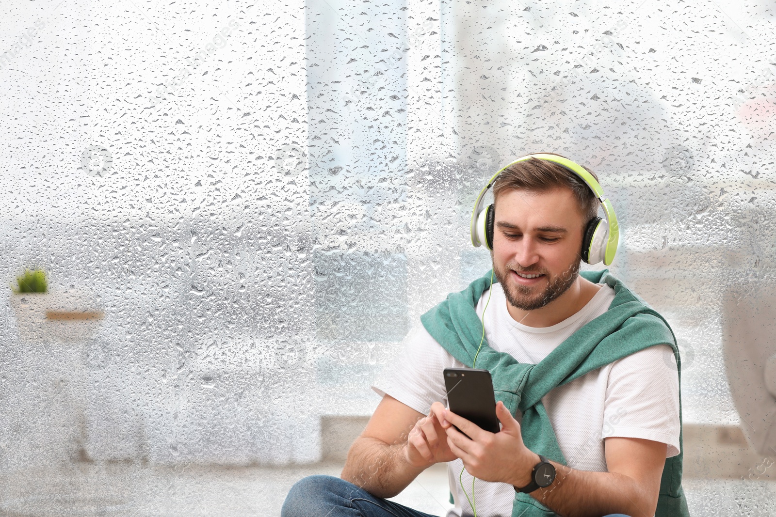 Image of Happy man listening to sounds of nature which making him feel calm. Double exposure of room and wet window on rainy day