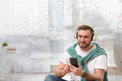 Image of Happy man listening to sounds of nature which making him feel calm. Double exposure of room and wet window on rainy day