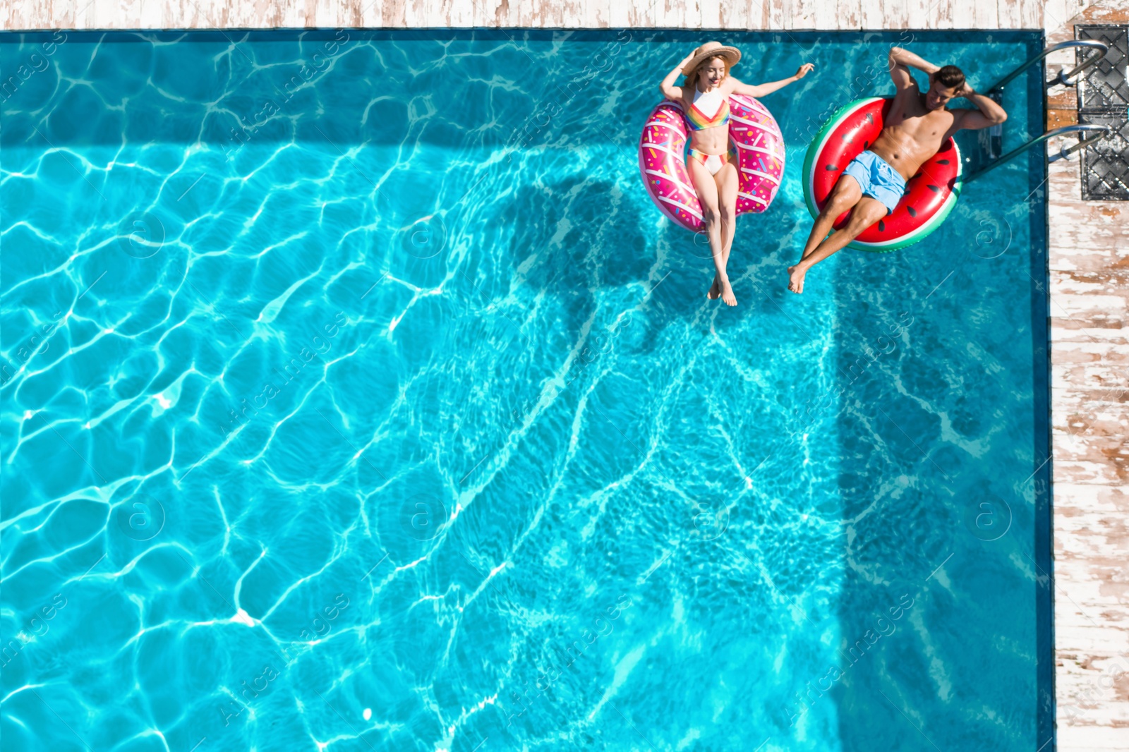 Image of Happy couple with inflatable rings in swimming pool, top view. Summer vacation