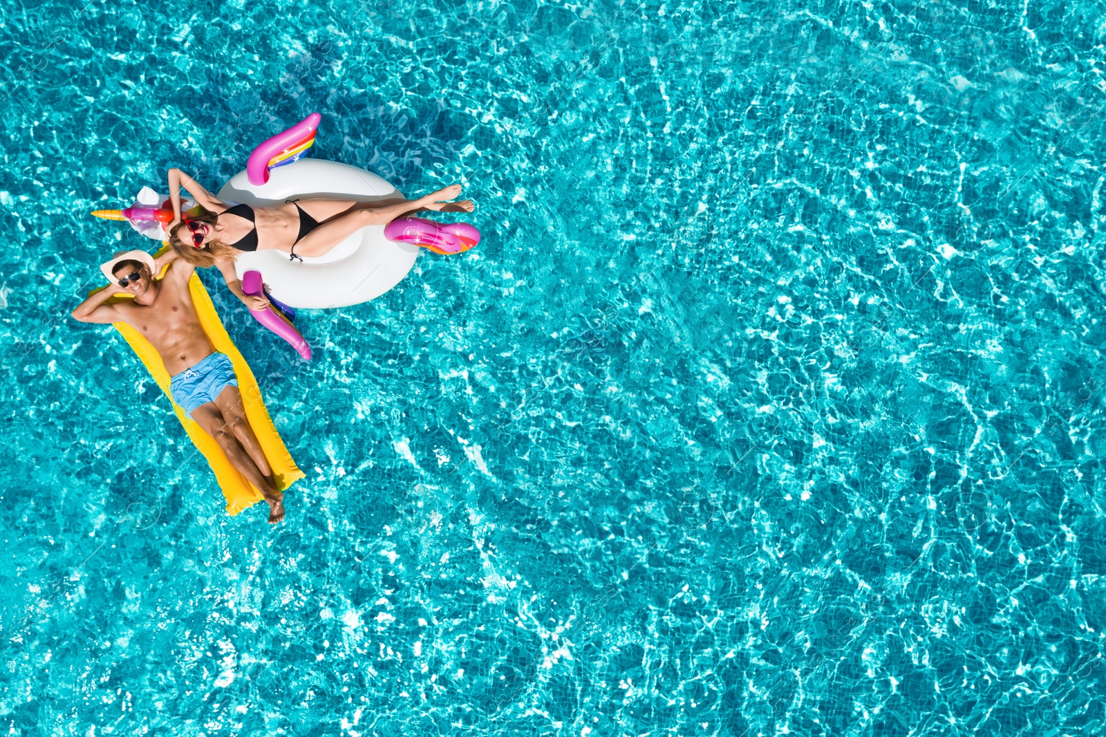 Image of Happy couple with inflatable ring and mattress in swimming pool, top view. Summer vacation