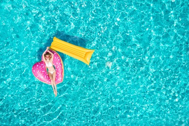 Image of Happy woman with inflatable mattress and ring in swimming pool, top view. Summer vacation