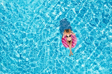 Image of Young happy woman with inflatable ring in swimming pool, top view. Summer vacation