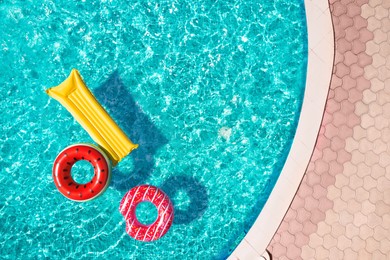 Image of Inflatable rings and mattress floating in swimming pool, top view. Summer vacation