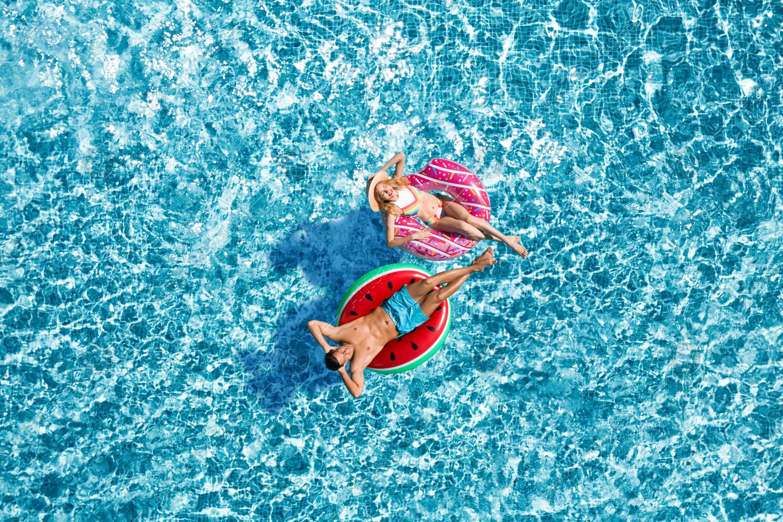 Image of Happy couple with inflatable rings in swimming pool, top view. Summer vacation