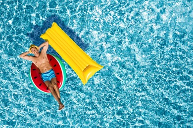 Image of Happy man with inflatable mattress and ring in swimming pool, top view. Summer vacation
