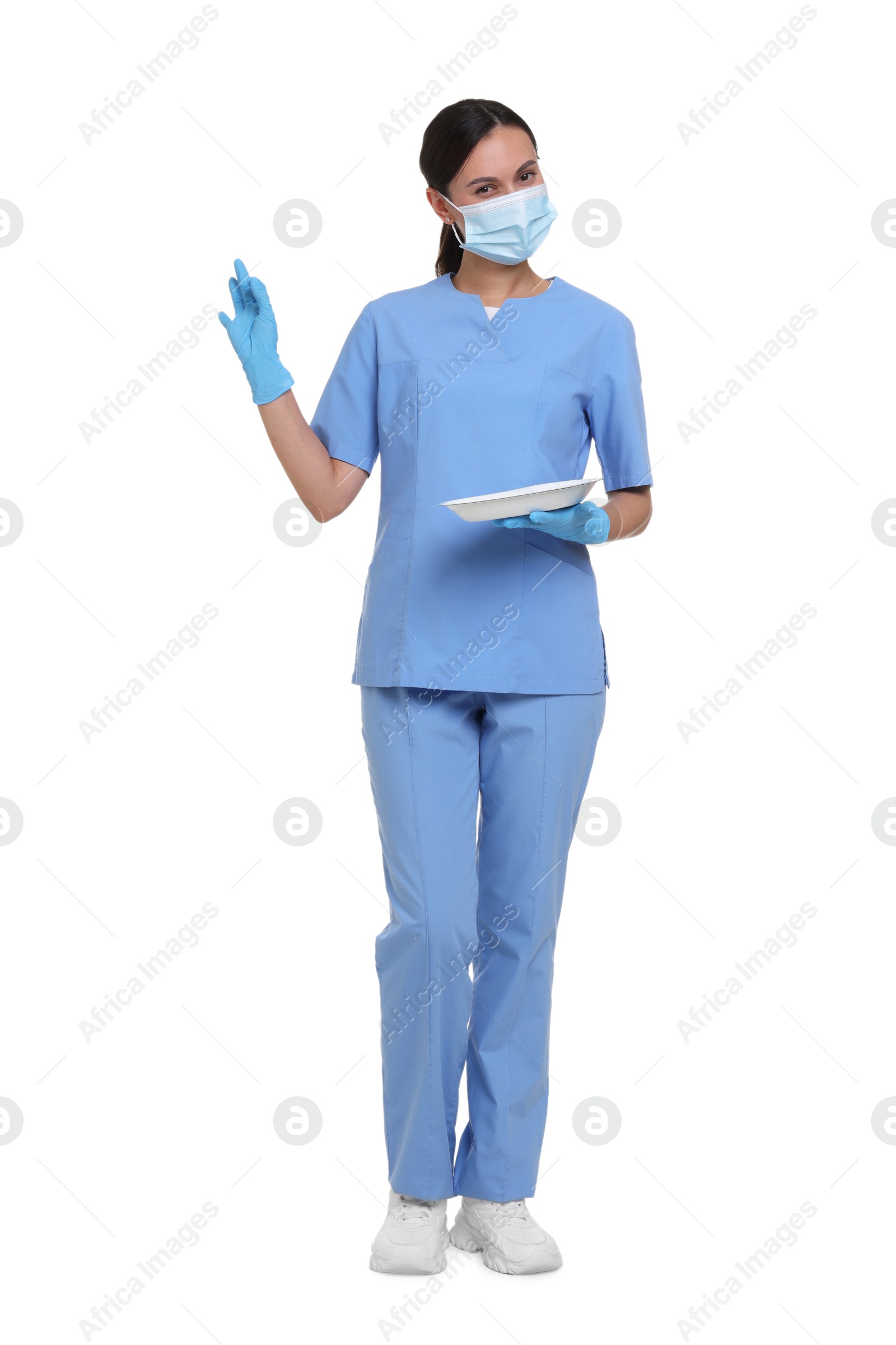 Nurse in uniform, medical mask and protective gloves with tray showing ok gesture on white background Photo of Nurse in uniform, medical mask and protective gloves with tray showing ok gesture on white background