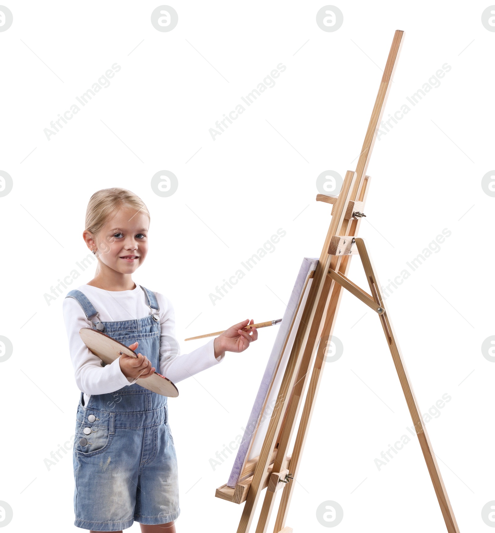 Photo of Choice of profession. Little girl with palette of paints and brush near easel pretending to be artist on white background