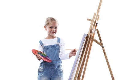 Photo of Choice of profession. Little girl with palette of paints and brush near easel pretending to be artist on white background