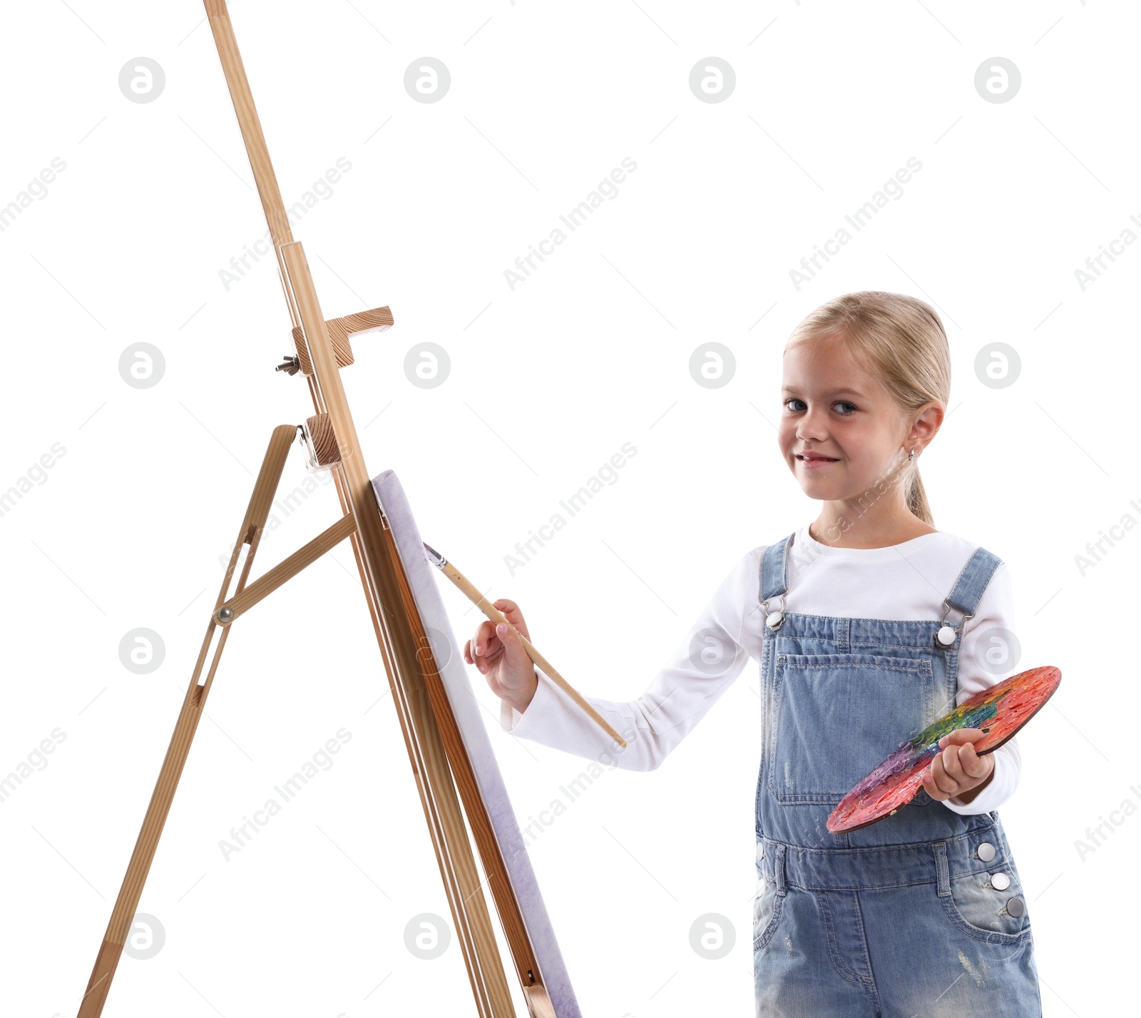 Photo of Choice of profession. Little girl with palette of paints and brush near easel pretending to be artist on white background