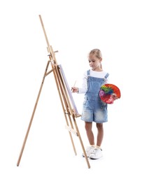 Photo of Choice of profession. Little girl with palette of paints and brush near easel pretending to be artist on white background