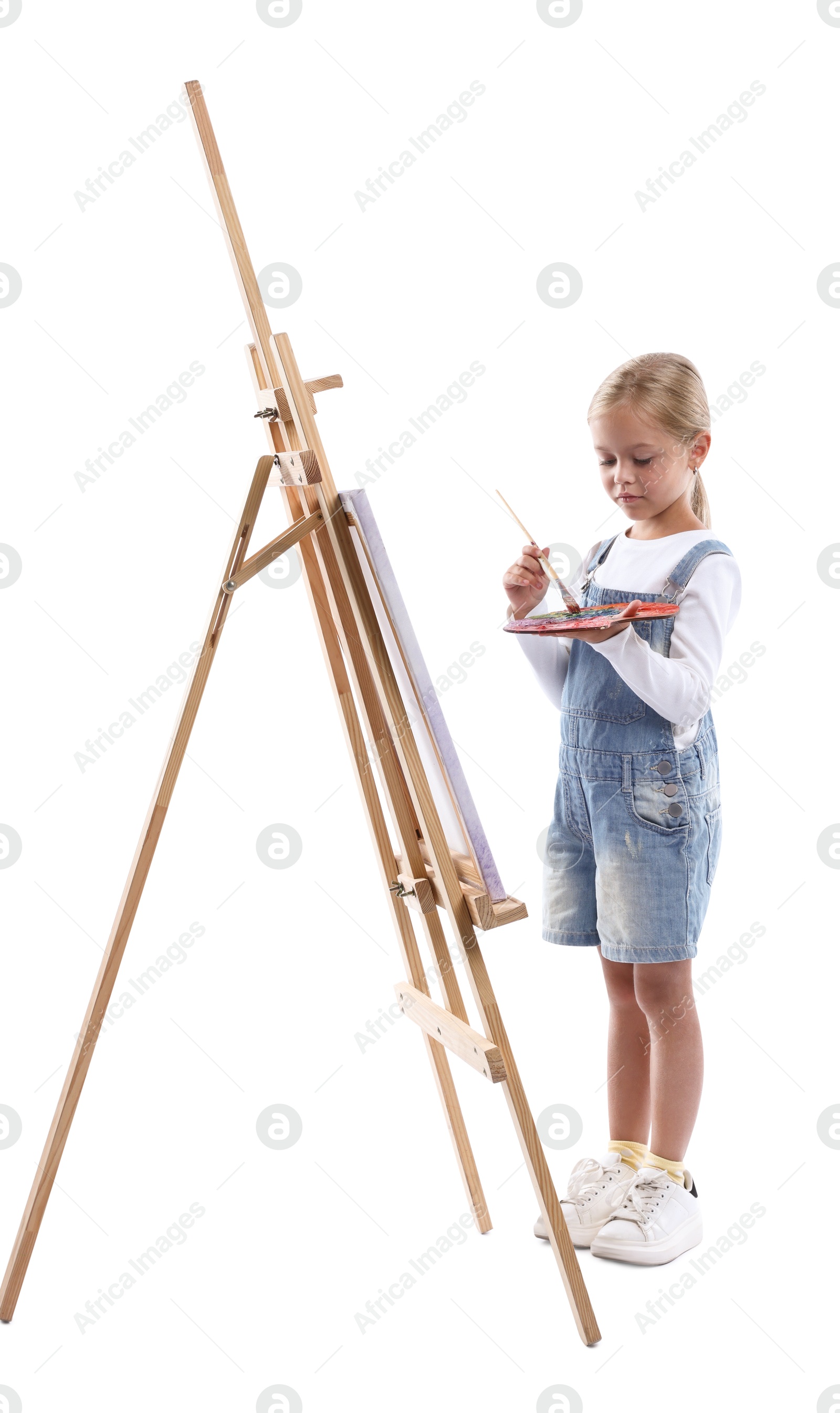 Photo of Choice of profession. Little girl with palette of paints and brush near easel pretending to be artist on white background