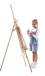 Photo of Choice of profession. Little girl with palette of paints and brush near easel pretending to be artist on white background