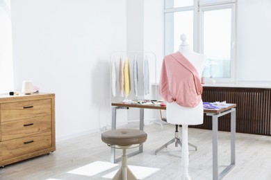 Photo of Female mannequin with fabric and sewing supplies in atelier