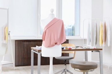 Photo of Female mannequin with fabric and sewing supplies in atelier