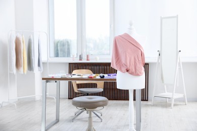 Photo of Female mannequin with fabric and sewing supplies in atelier
