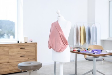 Photo of Female mannequin with fabric and sewing supplies in atelier