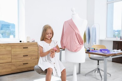 Photo of Choice of profession. Little girl with pin cushion pretending to be seamstress near mannequin in atelier