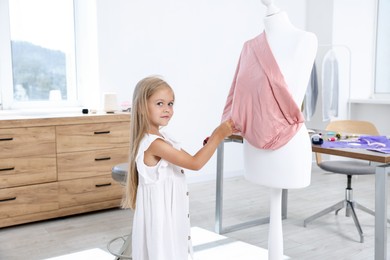 Photo of Choice of profession. Little girl sewing cloth on mannequin in atelier