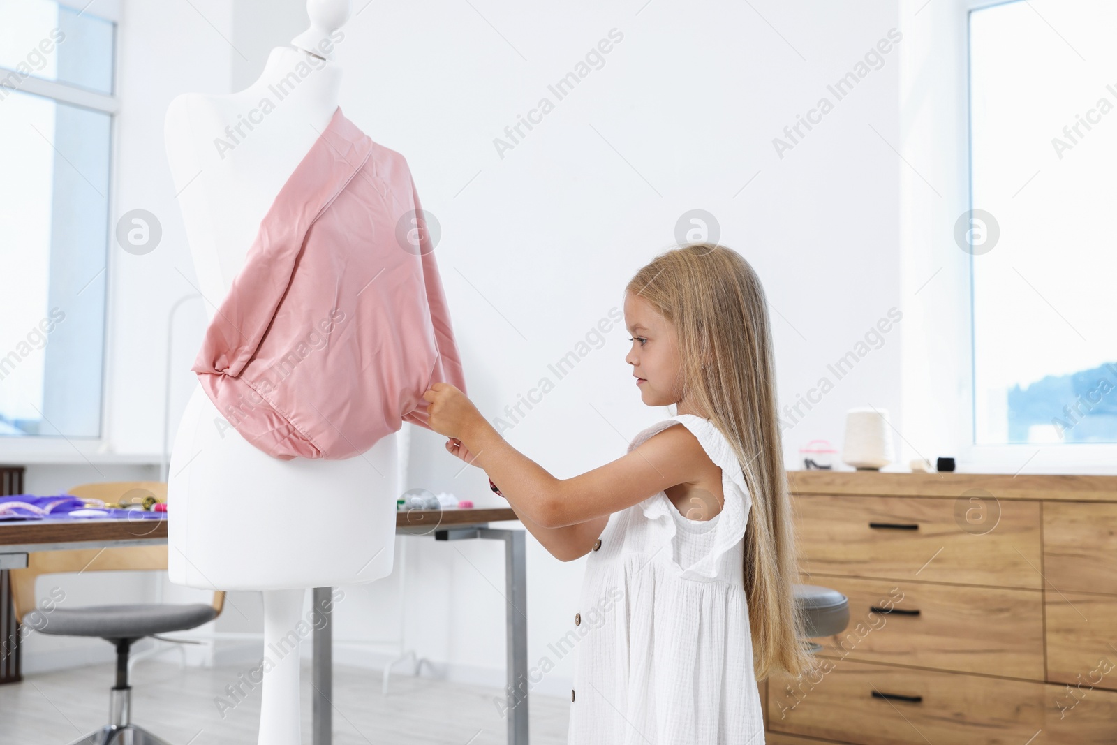 Photo of Choice of profession. Little girl sewing cloth on mannequin in atelier