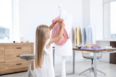 Photo of Choice of profession. Little girl with pin cushion pretending to be seamstress near mannequin in atelier