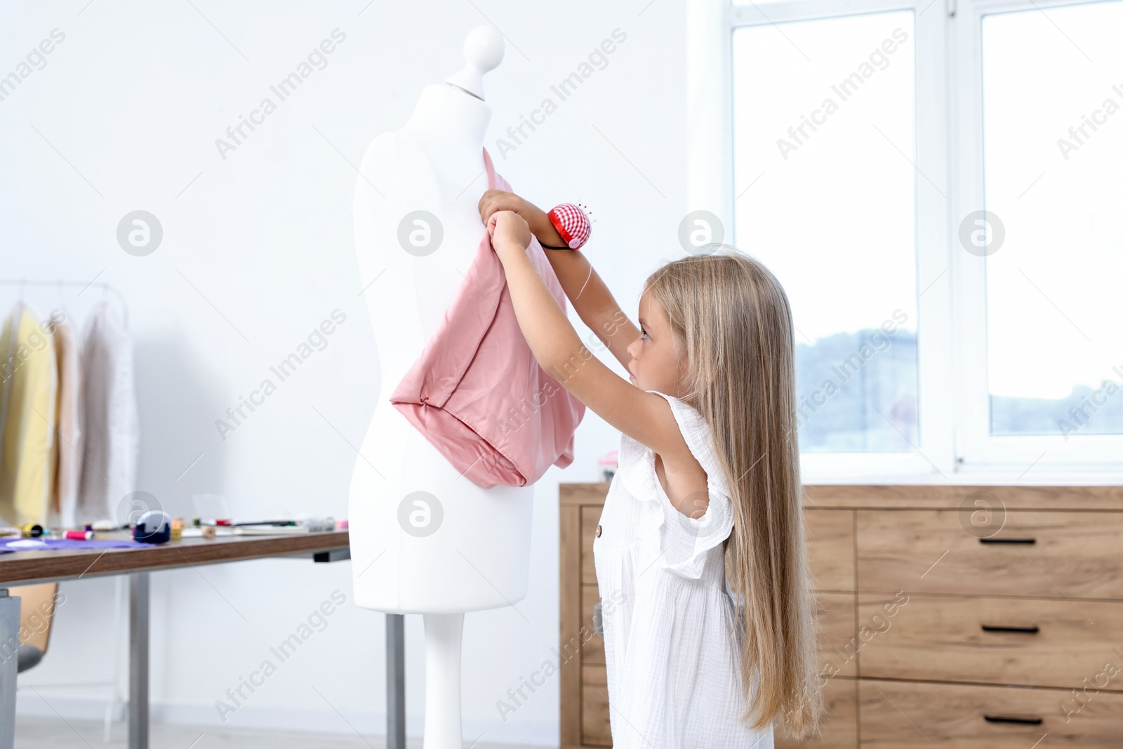 Photo of Choice of profession. Little girl with pin cushion pretending to be seamstress near mannequin in atelier