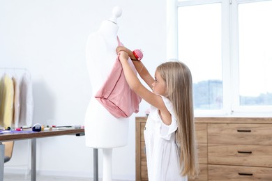 Photo of Choice of profession. Little girl with pin cushion pretending to be seamstress near mannequin in atelier