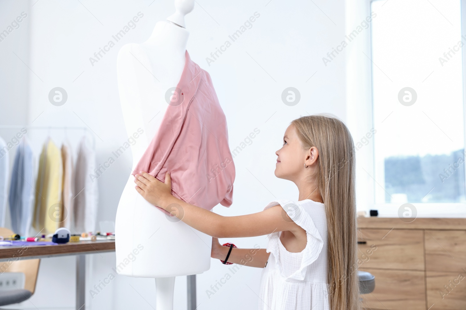 Photo of Choice of profession. Little girl pretending to be seamstress near mannequin in atelier