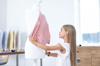 Photo of Choice of profession. Little girl pretending to be seamstress near mannequin in atelier